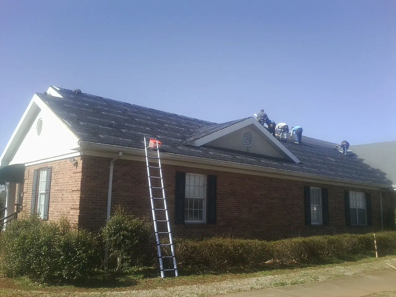 Crew tearing shingles off a brick ranch roof with a ladder set — Emergency Roof Repair work by our crew in Kirkersville