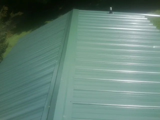New green metal panels meeting at the ridge of a roof — Flat Roof Repair work by our crew in Kirkersville