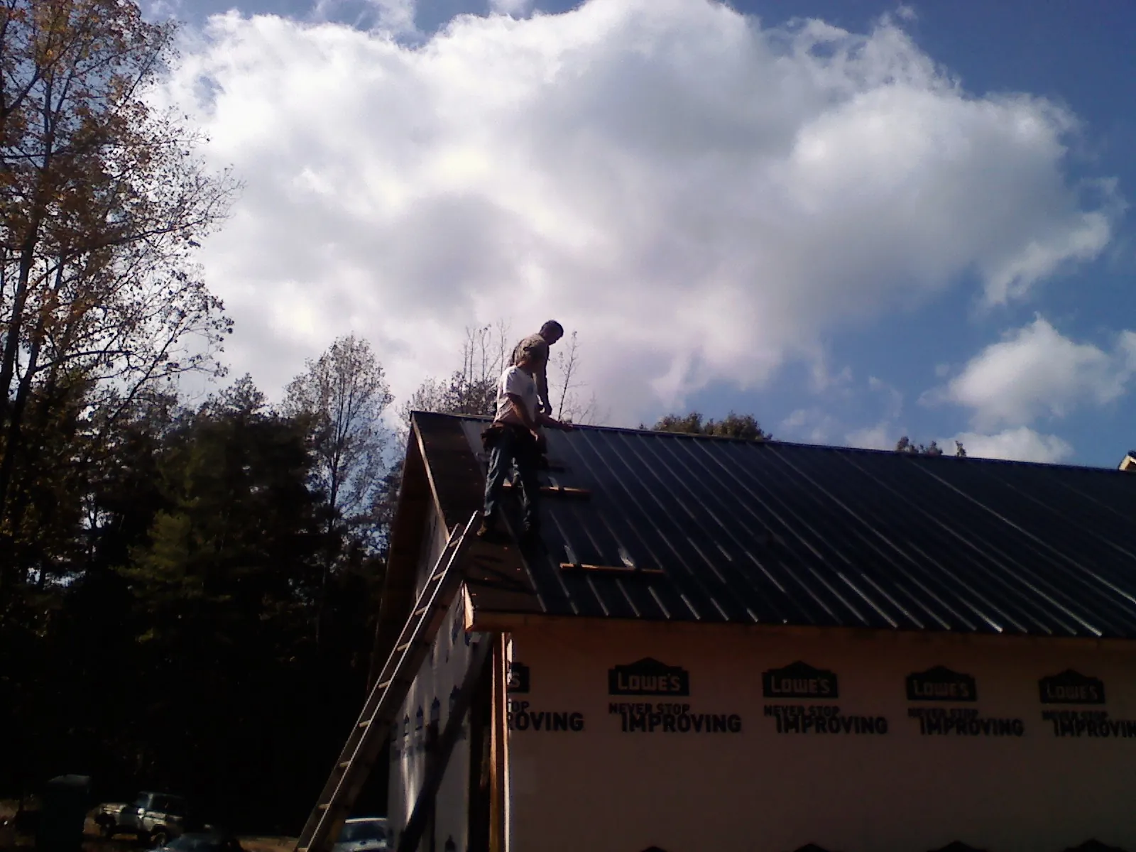 Roofer fastening dark metal panels high against a cloudy sky, from a Roof Inspection job in Kirkersville