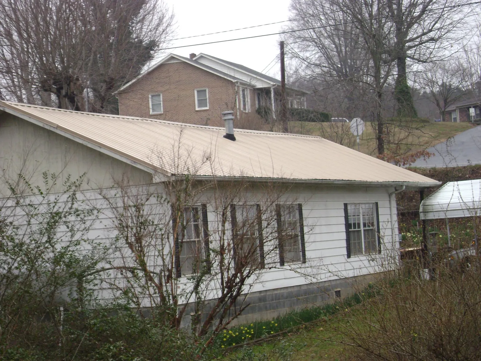 Tan metal roof on a white sided house set into a hillside — Commercial Roofing by Roofing Brothers in Kirkersville